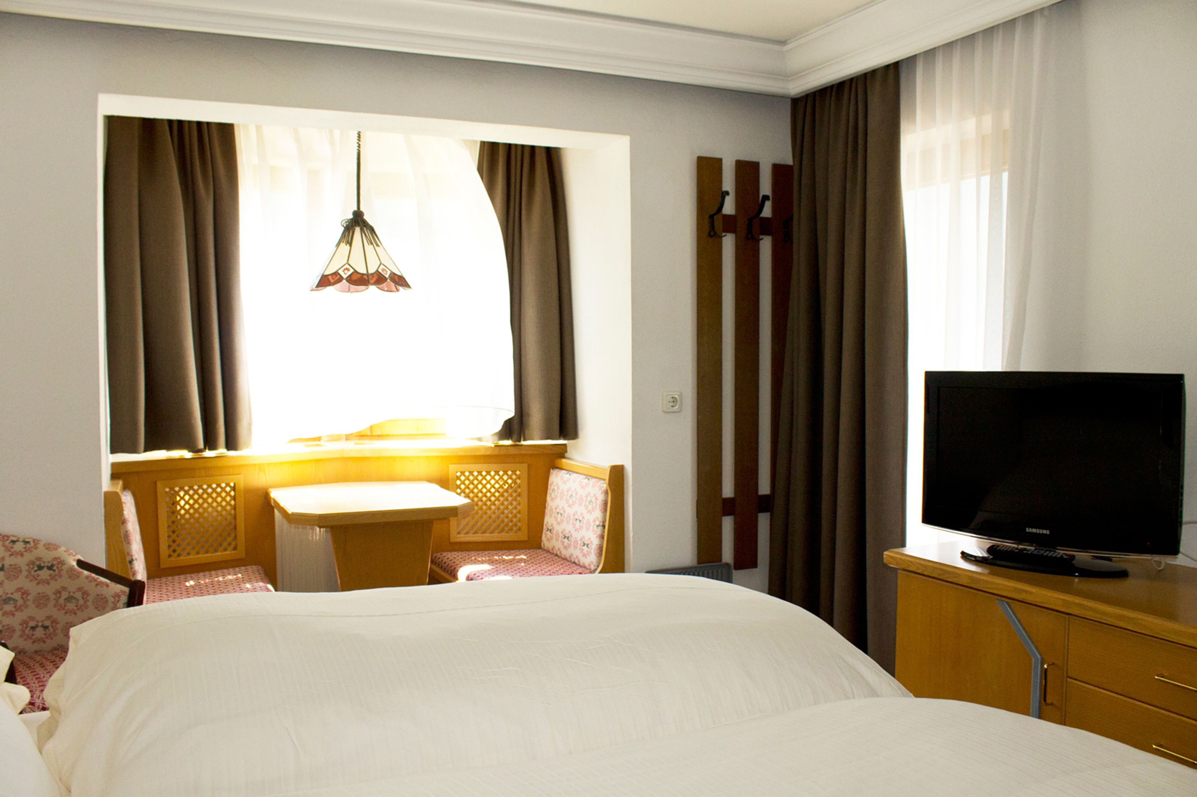 A hotel room with a bed, a small table, a chair, a television, and curtains.