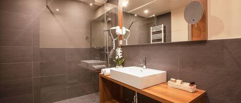 A modern bathroom with a large mirror, a wooden vanity, a white sink, and a shower area.