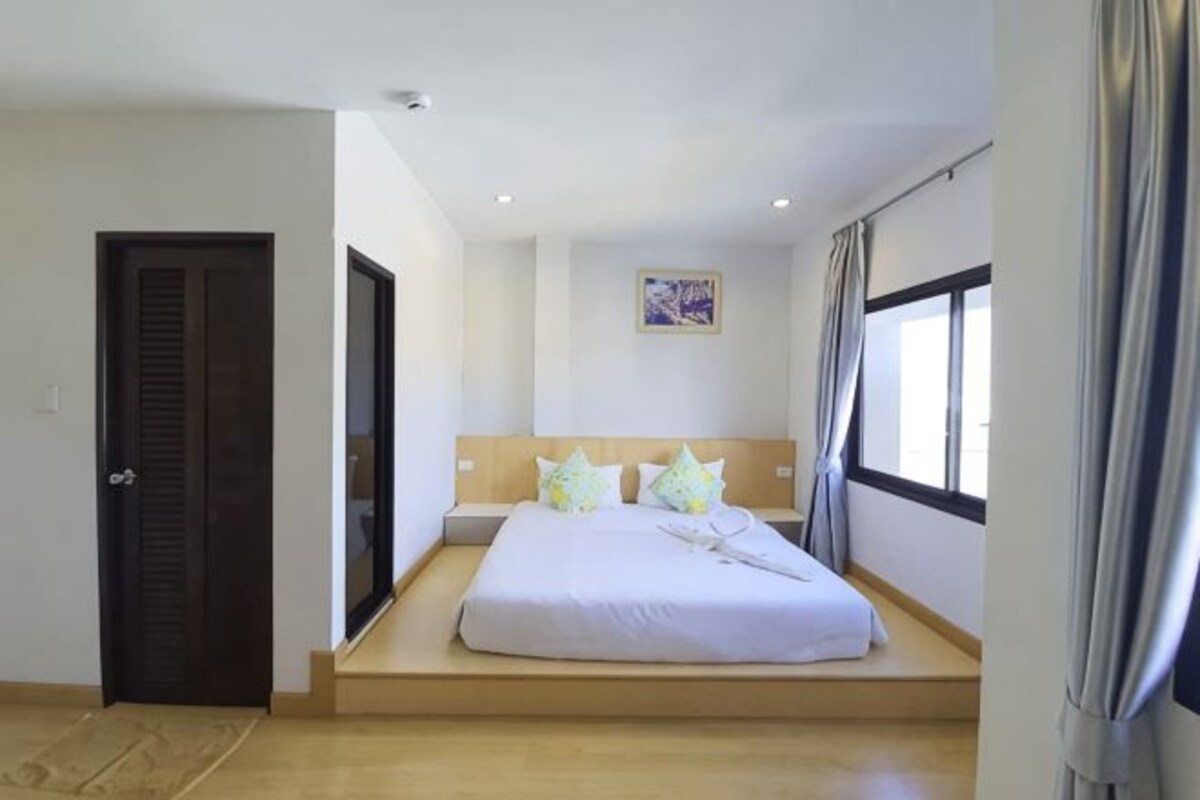 A bedroom with a bed, a door, a window, and a painting on the wall.