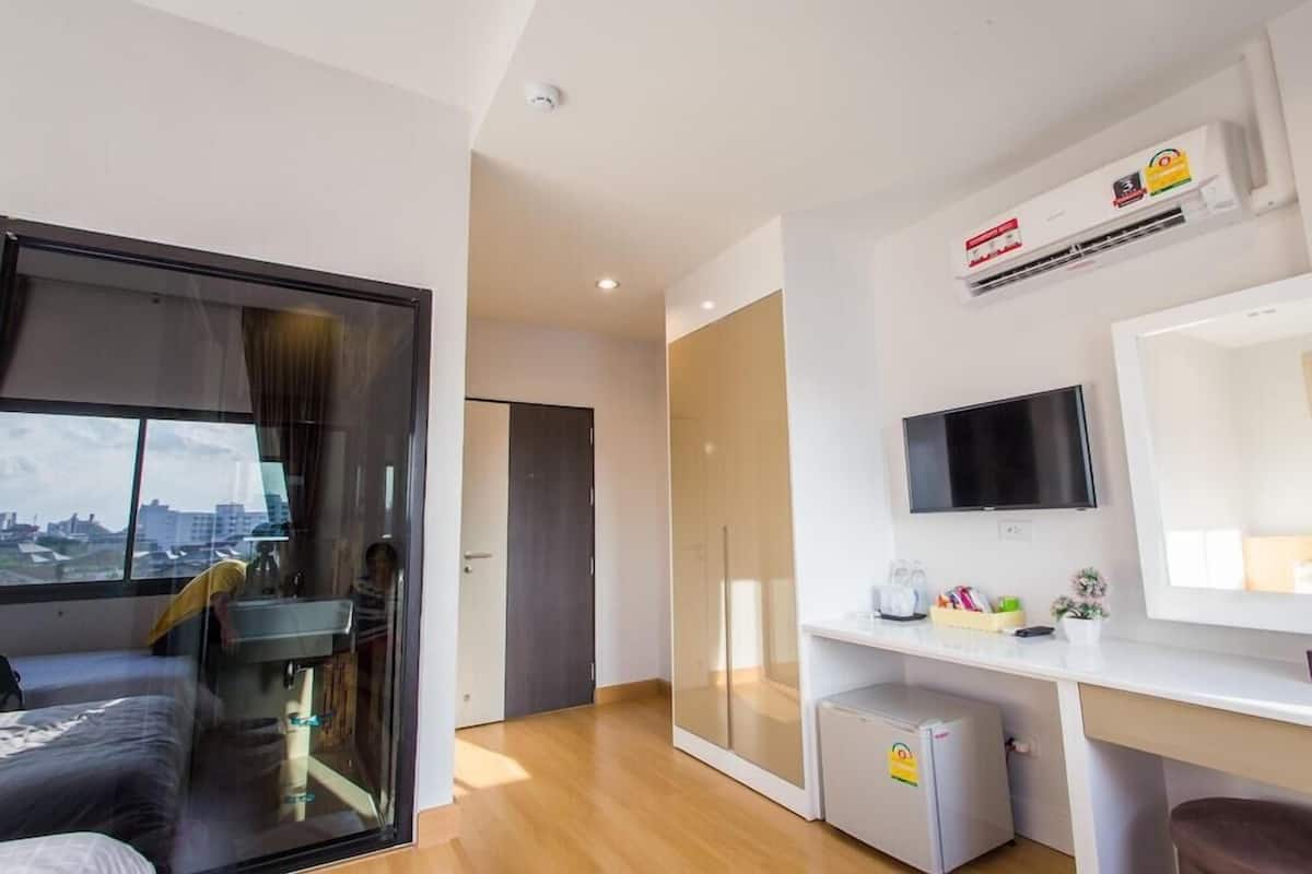 A modern hotel room with a bed, a desk, a television, and a view of the city through a large window.