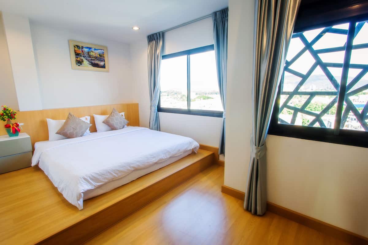 A hotel room with a bed, a nightstand, a window with curtains, and a painting on the wall.