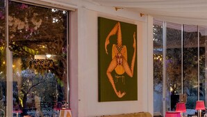 Een eetruimte met gedekte tafels, roze lampen, wijnglazen en een schilderij aan de muur.