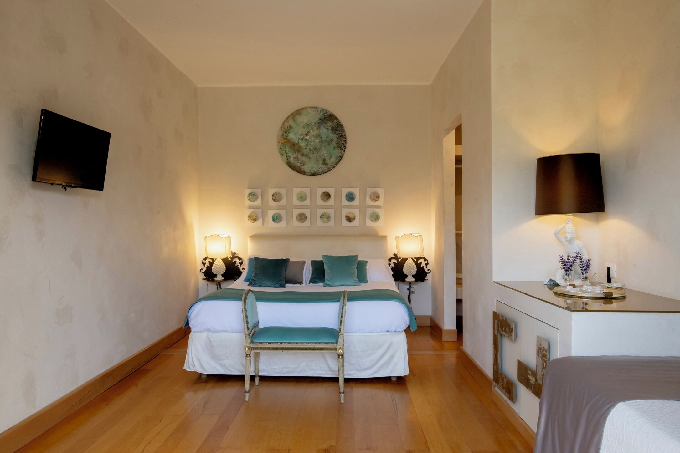 Habitación de hotel con una cama, lámparas de noche, un televisor, un adorno en la pared y una pequeña mesa con una estatua.