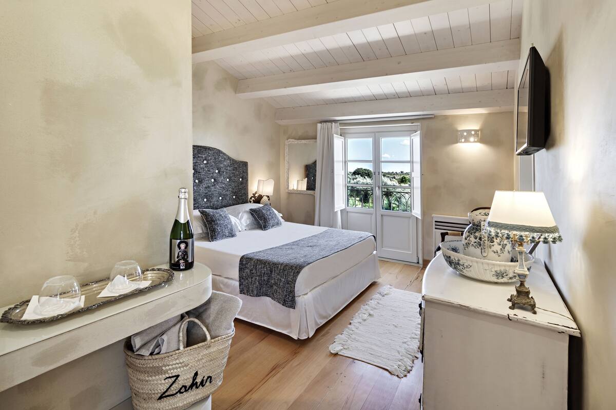 Ein Schlafzimmer mit Bett, Nachttisch, Lampe und Blick ins Freie.
