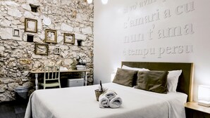 A bedroom with a stone wall, a bed with white bedding, and a wall with text. - B&B Siracusa (Syracuse)
