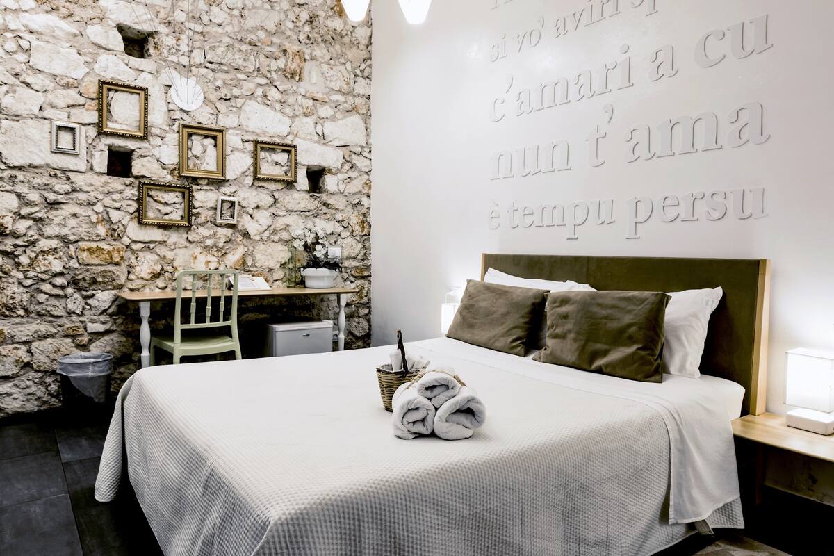 A bedroom with a stone wall, a bed with white bedding, and a wall with text.