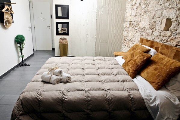 A bedroom with a large bed, a wooden headboard, and a stone wall. - B&B Siracusa (Syracuse)