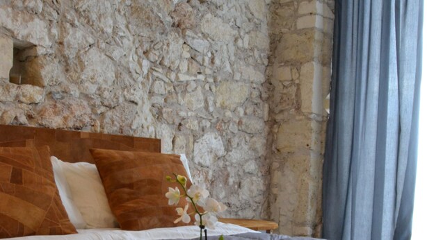 A bedroom with a stone wall, a bed with a wooden headboard, a tray with a plant, and a window with curtains. - B&B Siracusa (Syracuse)