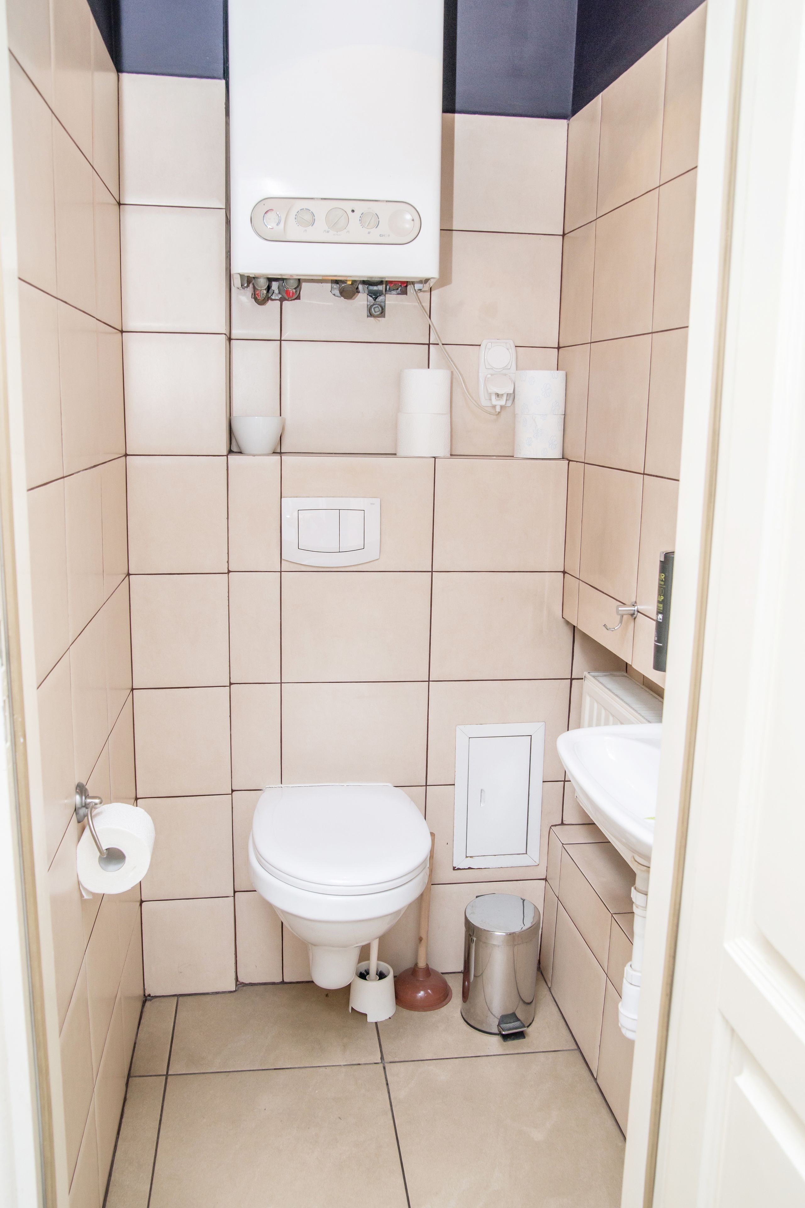 A small, tiled bathroom with a toilet, sink, and trash can.