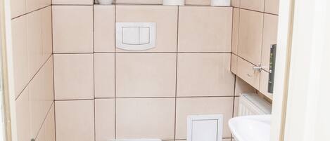 A small, tiled bathroom with a toilet, sink, and trash can.