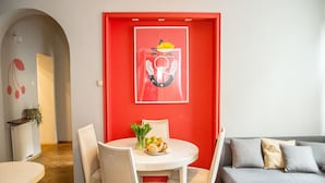Een moderne woonkamer met een rode accentmuur, een ronde eettafel met stoelen en een grijze bank.