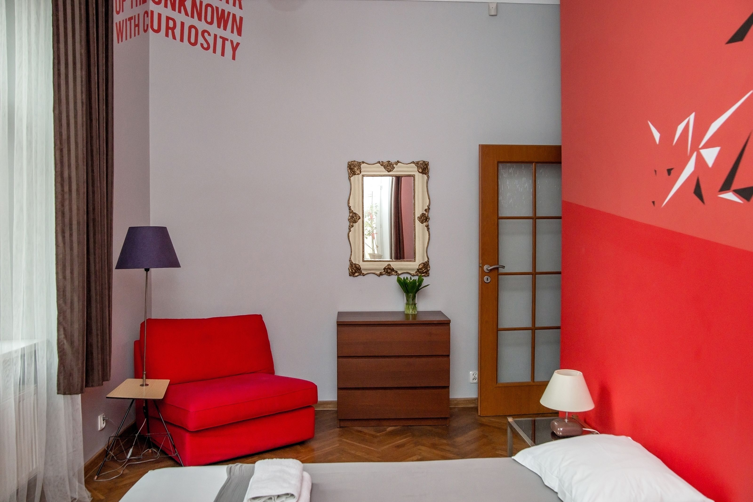 A hotel room with a red sofa, a wooden dresser, a mirror, and a bed.