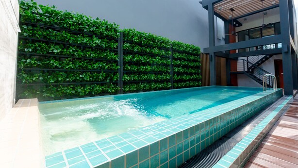 A modern indoor swimming pool with a tiled edge, surrounded by a green wall and wooden deck flooring. - Recenta Style Phuket Town (Phuket)
