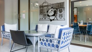 A dining area with wicker chairs and a glass table, a wall mural of a panda, and a view through a glass door. - Recenta Style Phuket Town (Phuket)