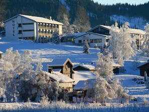 A hotel with a modern building and traditional cabins, surrounded by snow-covered trees and a mountainous backdrop. - Morgedal Hotell - Unike Hoteller (Kviteseid)