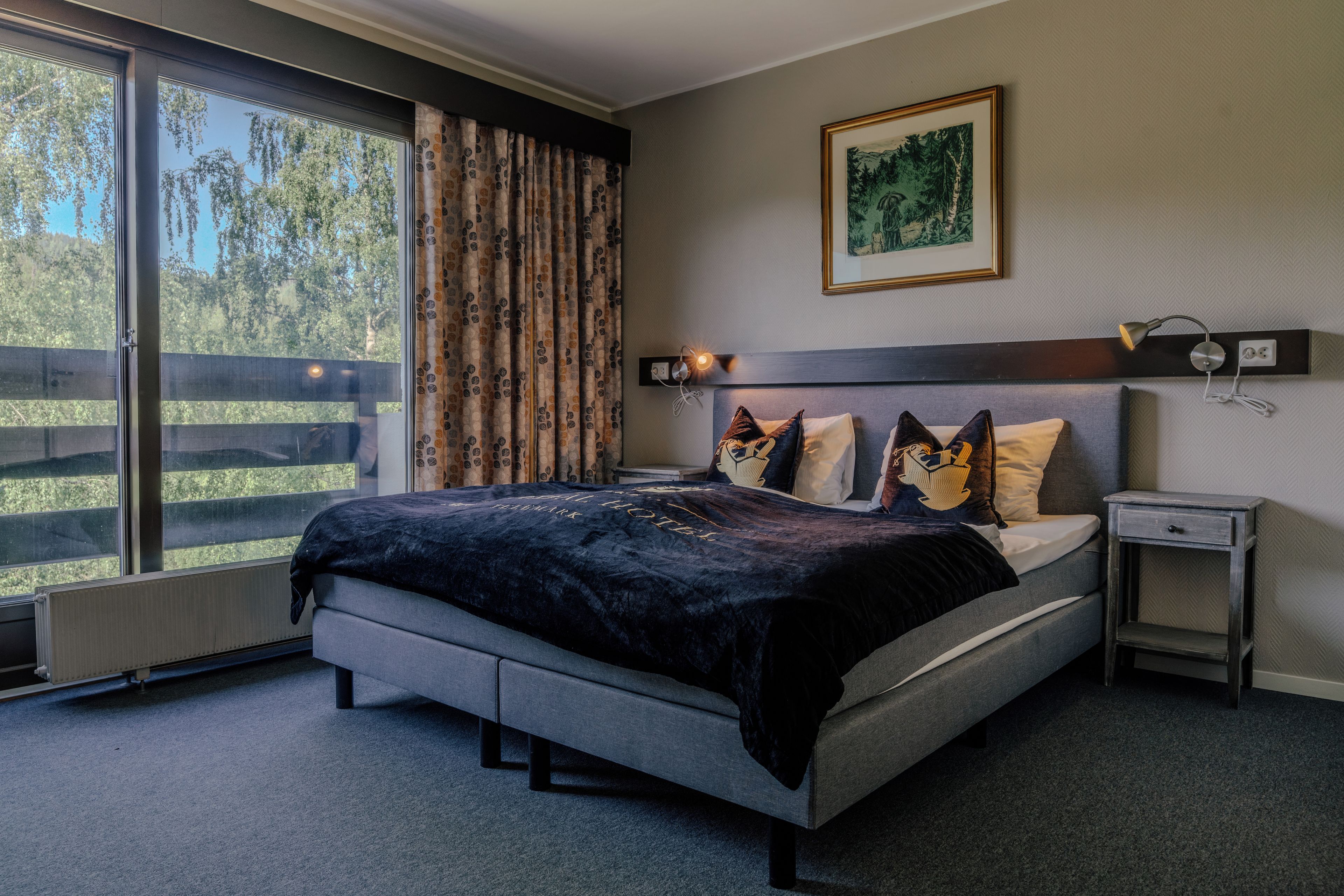 Een slaapkamer met een groot bed, een nachtkastje, een wandlamp en een raam met gordijnen.