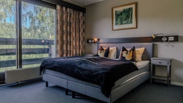 Een slaapkamer met een groot bed, een nachtkastje, een wandlamp en een raam met gordijnen.