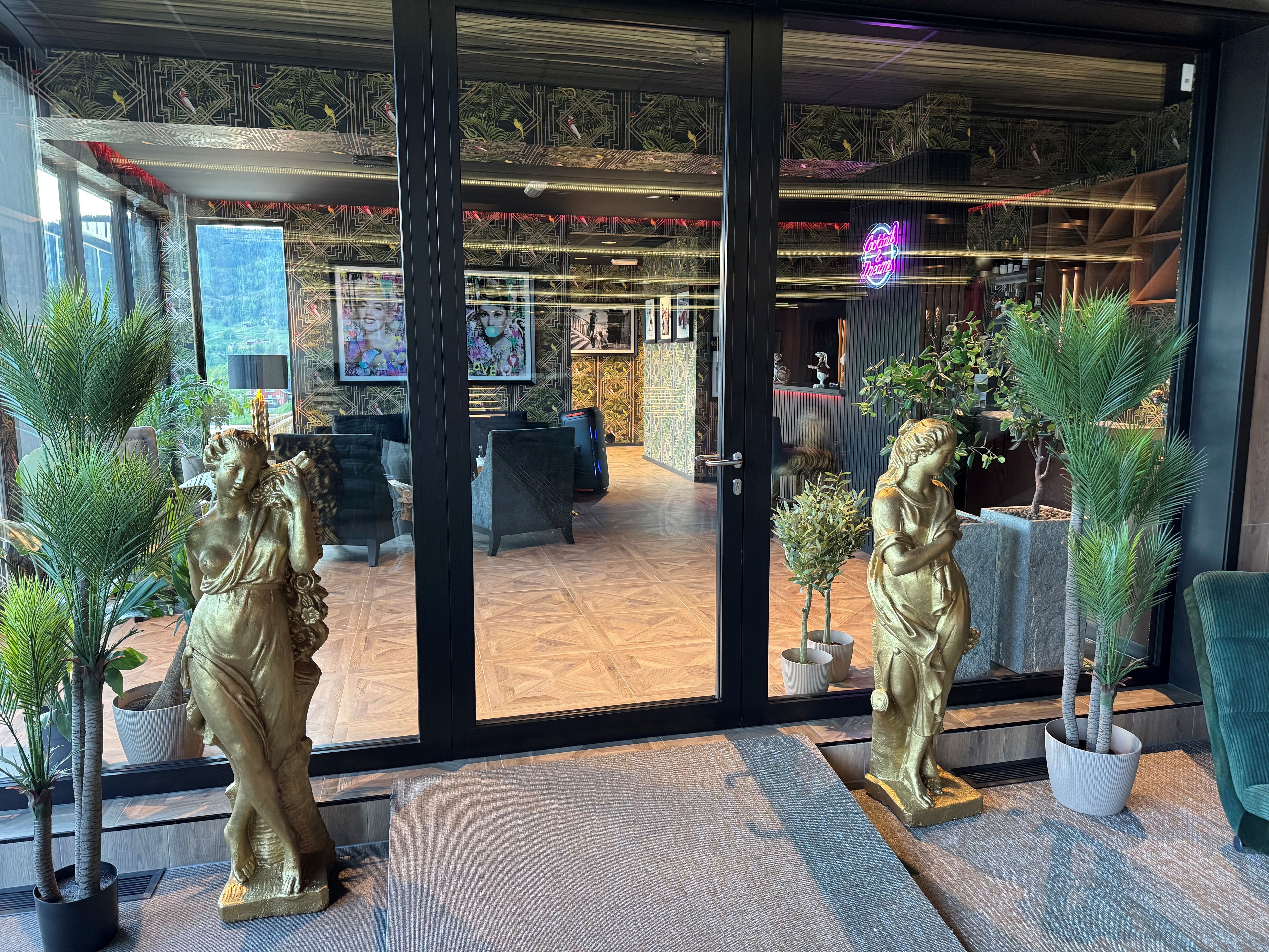 A modern interior with a glass door entrance, potted plants, and a neon sign.