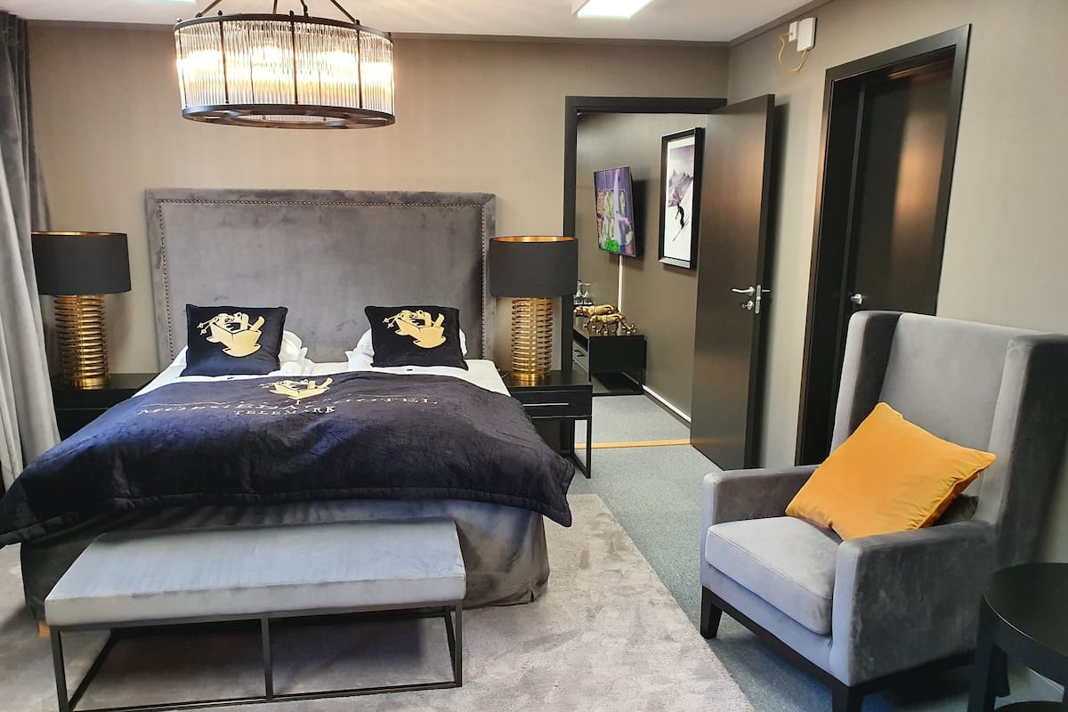 Un dormitorio moderno con una cama grande, lámparas de noche, un sillón tapizado en gris y una araña.