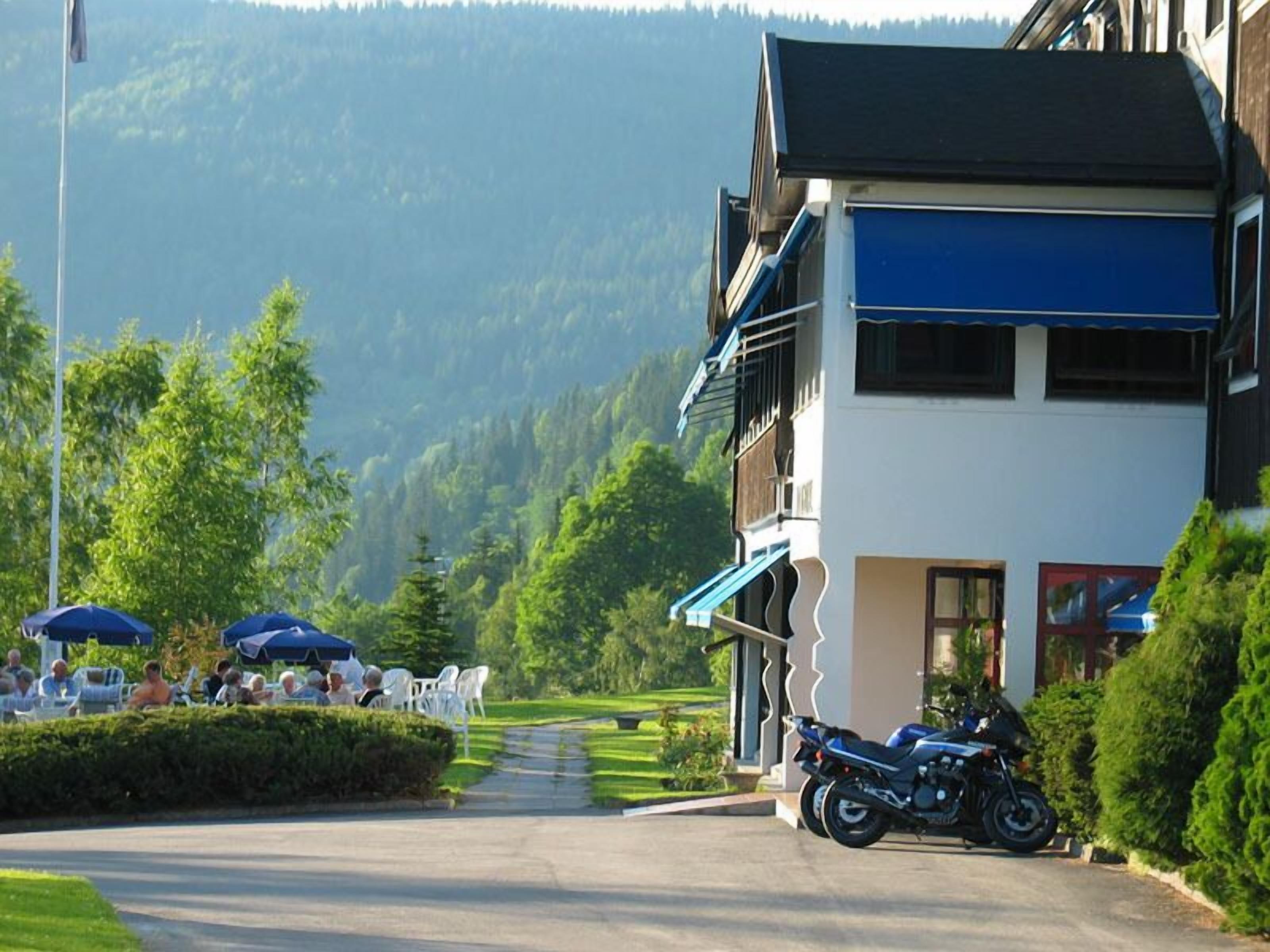 Un edificio con un balcone, una motocicletta parcheggiata e un gruppo di persone sedute ai tavoli all'esterno.