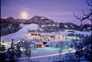 Un hotel grande y de varios pisos, con un diseño moderno, ubicado en una colina nevada rodeada de árboles.