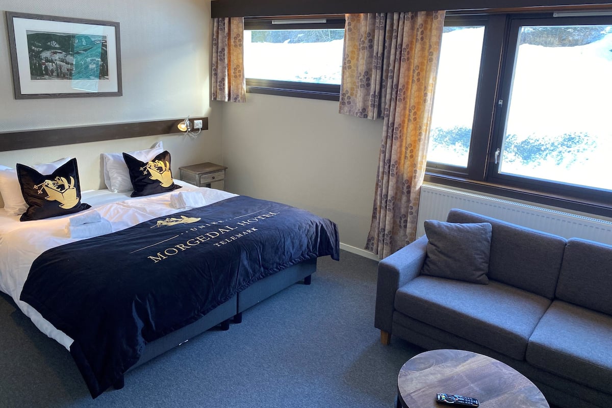Una habitación de hotel con cama, sofá, una mesita y ventana con cortinas.