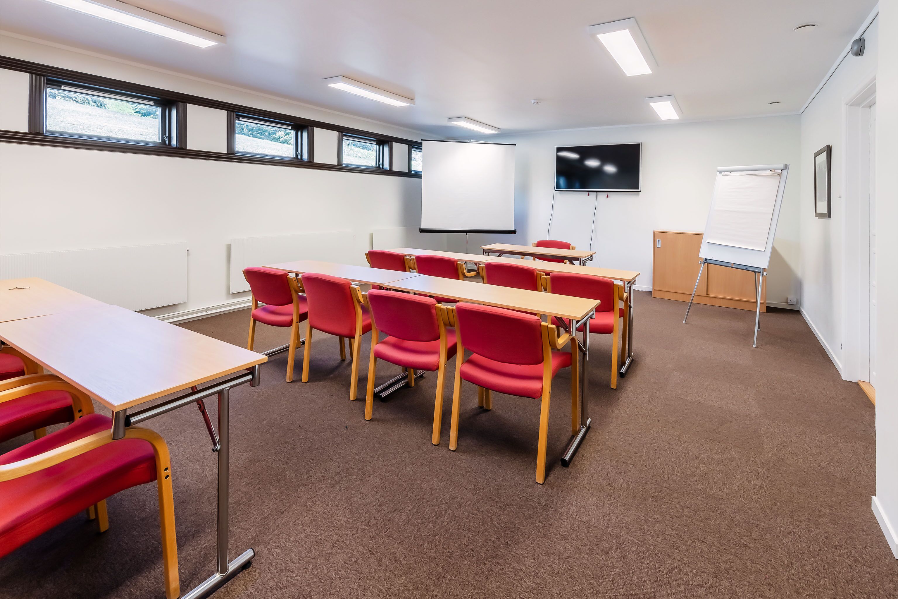 A classroom with red chairs, a whiteboard, and a projector screen.