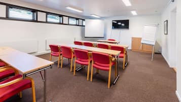 A classroom with red chairs, a whiteboard, and a projector screen.