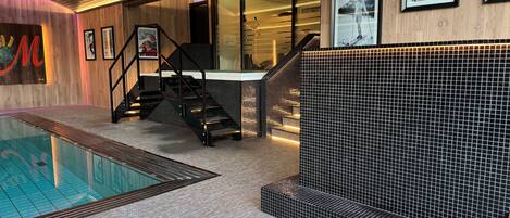 A modern indoor pool area with a glass barrier, a staircase, and a tiled wall.