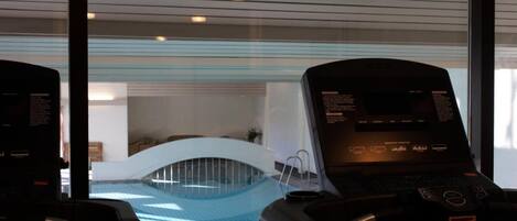 A modern indoor swimming pool with a curved ceiling and a view of a lounge area.
