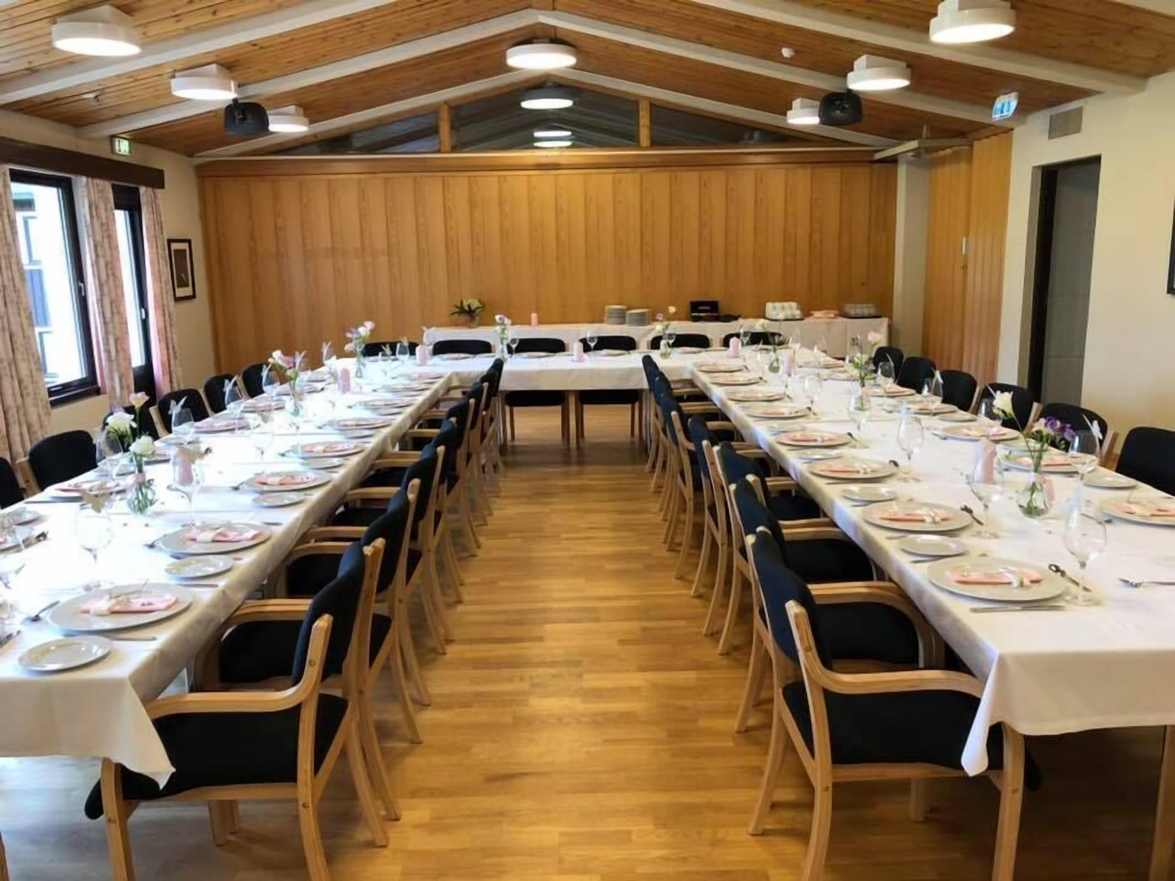 A long dining table set with white tablecloths, wooden chairs, and neatly arranged table settings.