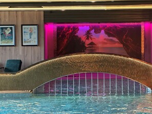 A swimming pool with a decorative arch, framed by a mural depicting a tropical scene with palm trees and a sunset. - Morgedal Hotell - Unike Hoteller (Kviteseid)