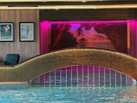 Una piscina con un arco decorativo, enmarcada por un mural que representa una escena tropical con palmeras y una puesta de sol.