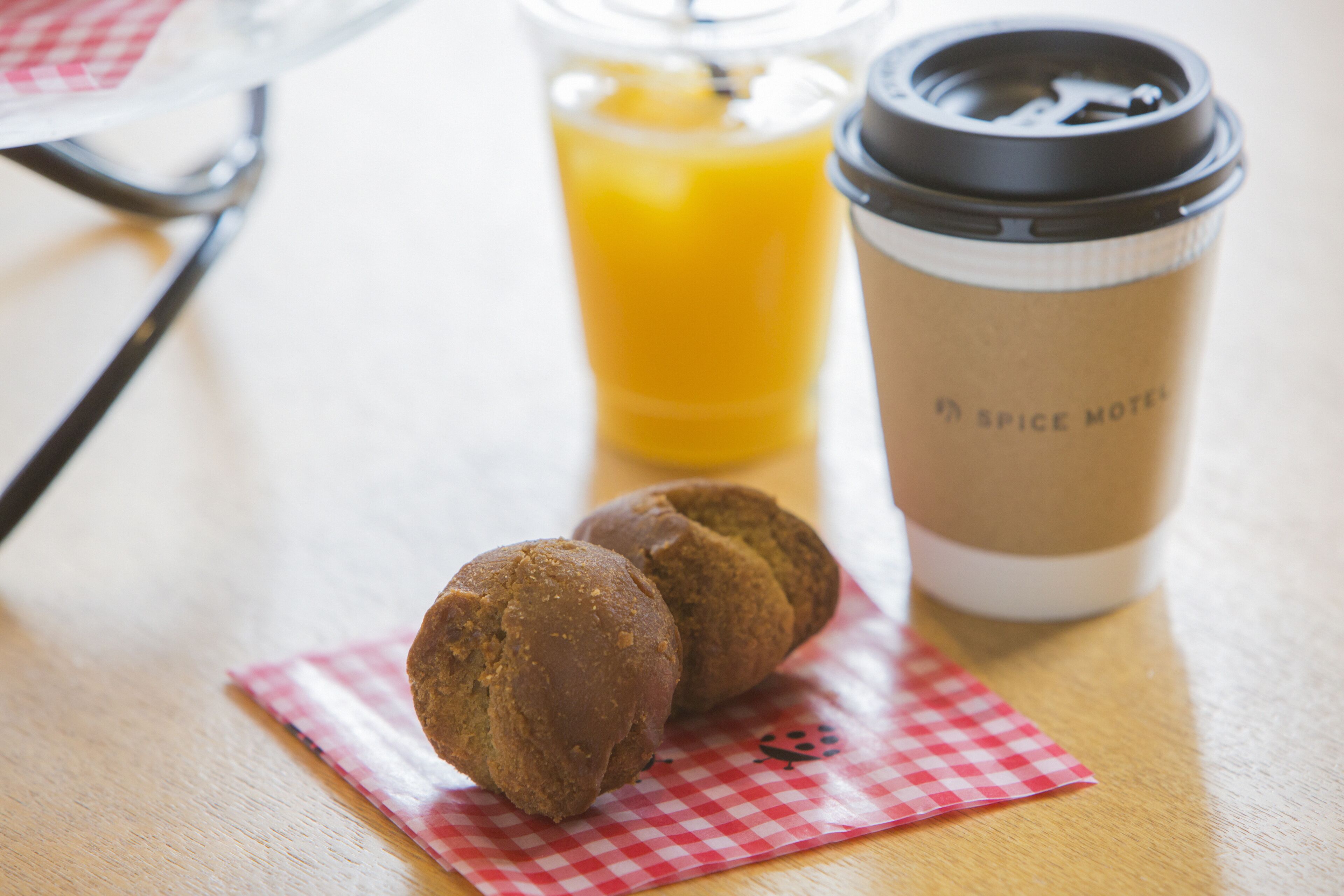 A table with a coffee cup, a glass of orange juice, and two muffins on a red and white checkered napkin.