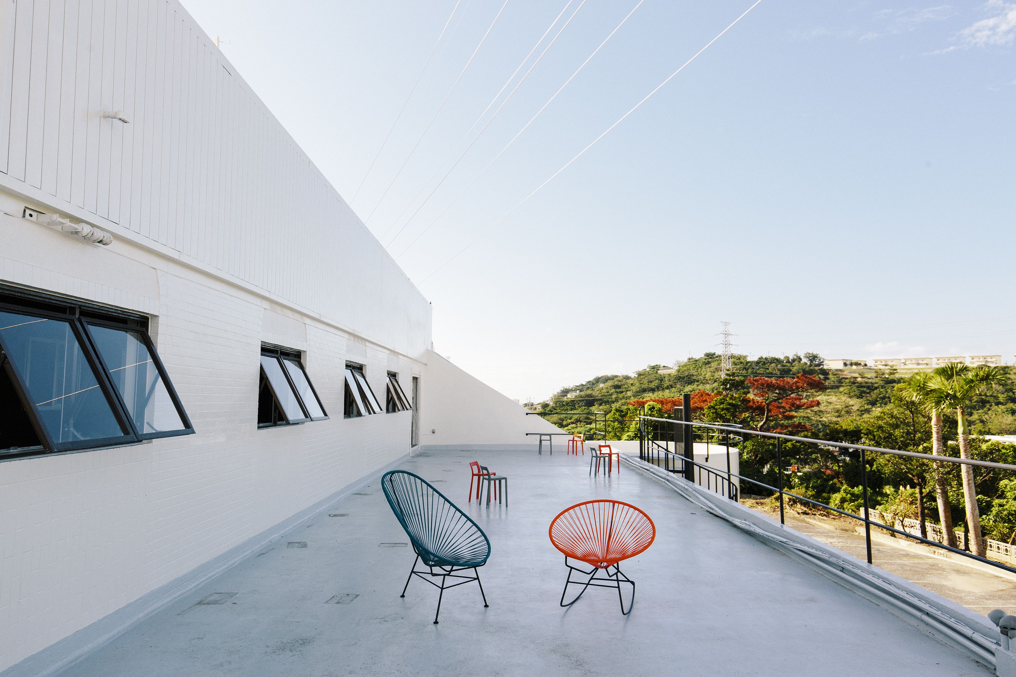 A rooftop terrace with two chairs, a table, and a railing overlooking a hilly landscape.