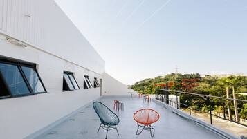 A rooftop terrace with two chairs, a table, and a railing overlooking a hilly landscape.