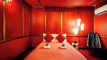 Una habitación de hotel con una decoración en rojo y dorado, una cama con ropa de cama a rayas, dos almohadas, una mesita de noche con una lámpara y un sillón de cuero negro.