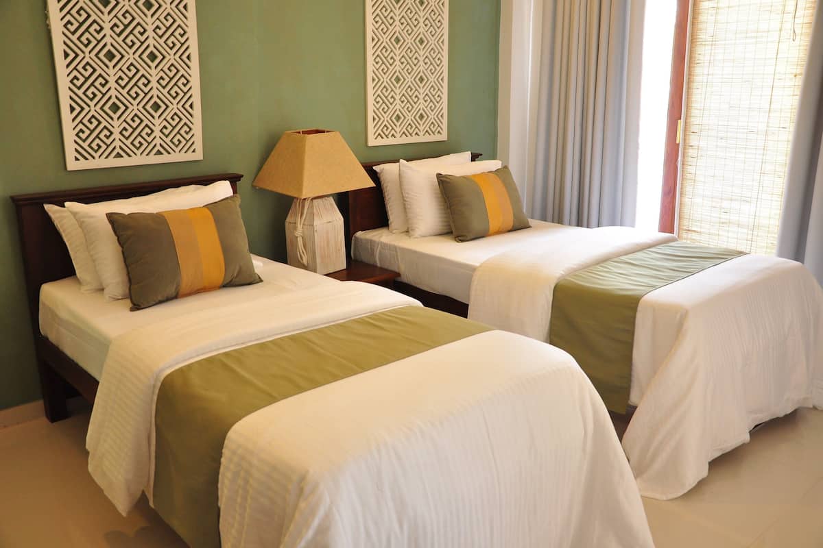 A hotel room with two beds, a nightstand with a lamp, and decorative wall panels.
