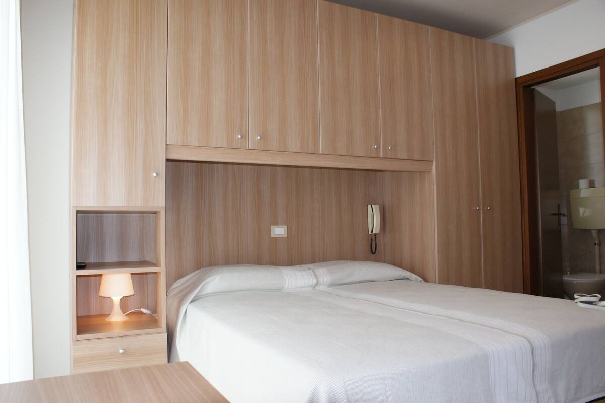 A bedroom with a bed, a bedside table with a lamp, a wardrobe, and a telephone.