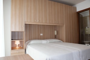 Ein Schlafzimmer mit einem Bett, einem Nachttisch mit Lampe, einem Kleiderschrank und einem Telefon.