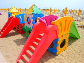 Ein Strandspielplatz mit bunten Kunststoffkonstruktionen, darunter Rutschen und Kletterelemente.
