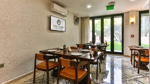 Une salle à manger d’hôtel avec des tables dressées pour le service, un panneau encadré accroché au mur et une vue sur l’extérieur grâce à de grandes fenêtres.