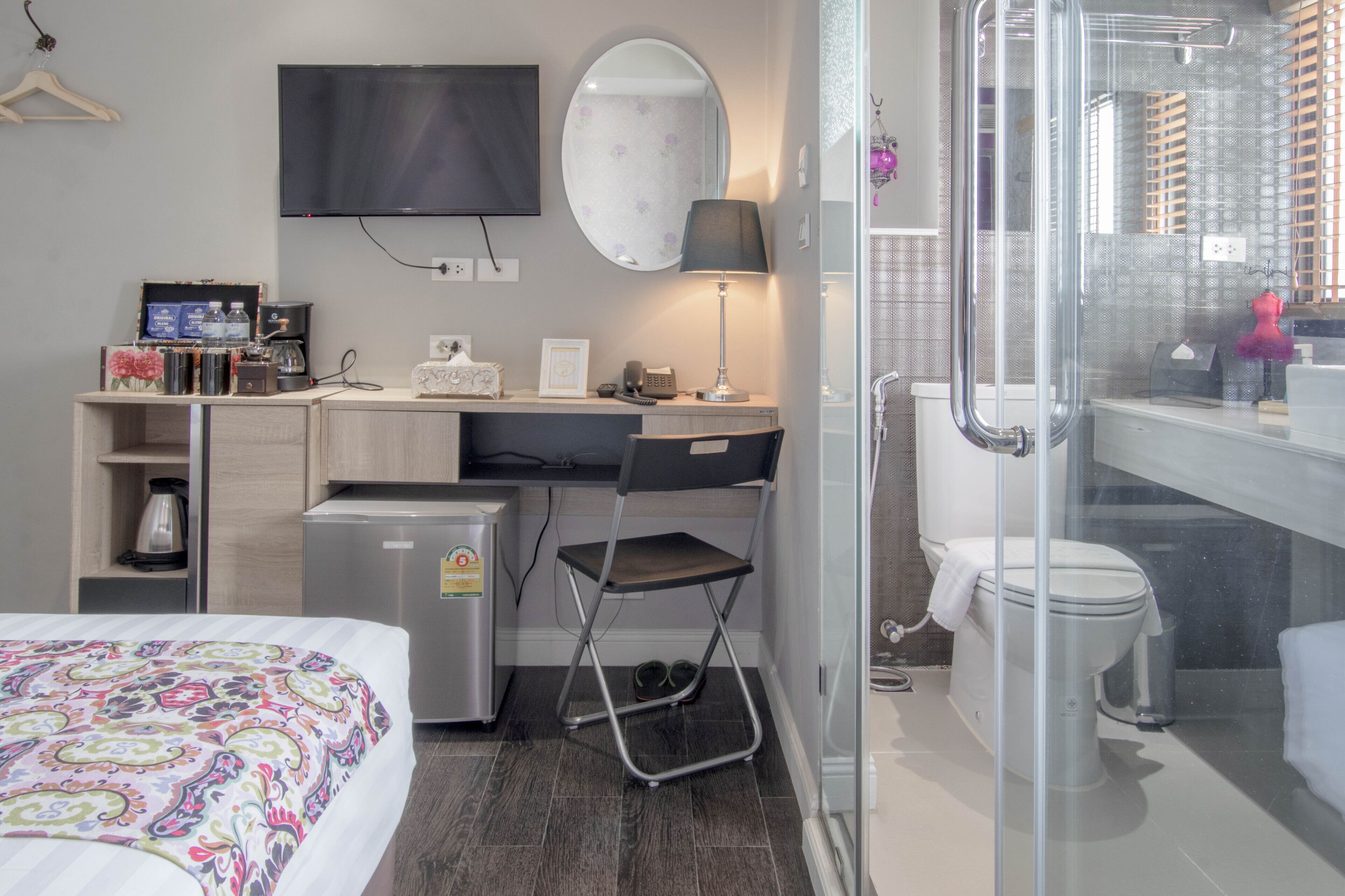 Habitación de hotel compacta con cama, escritorio, silla, televisor y zona de ducha.