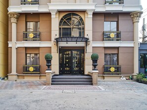 A multi-story building with a central entrance featuring a black door with ornate gold detailing, flanked by two large planters. - The Star of Sathorn (Bangkok)