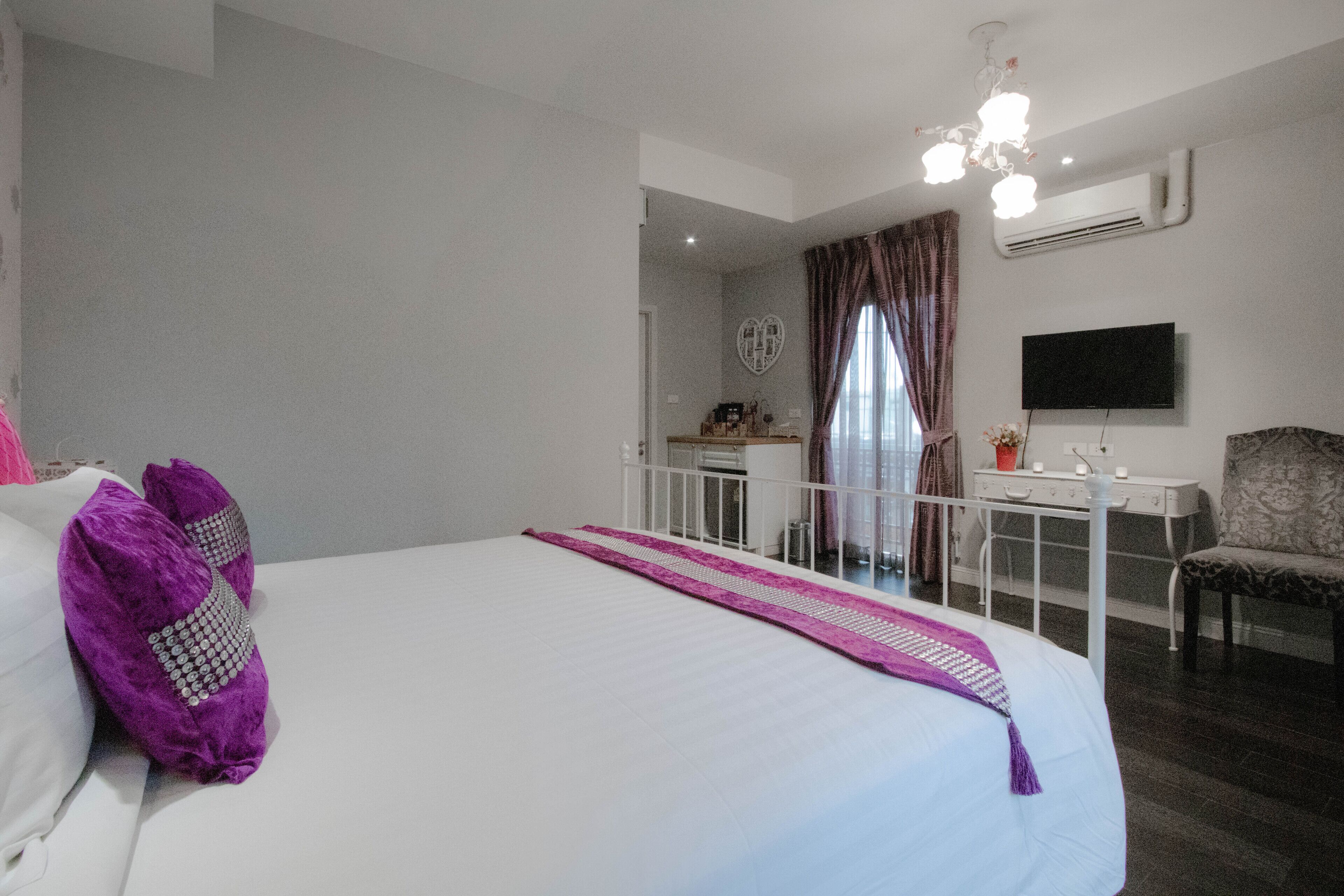 A hotel room with a large bed, a desk, a chair, and a TV mounted on the wall.