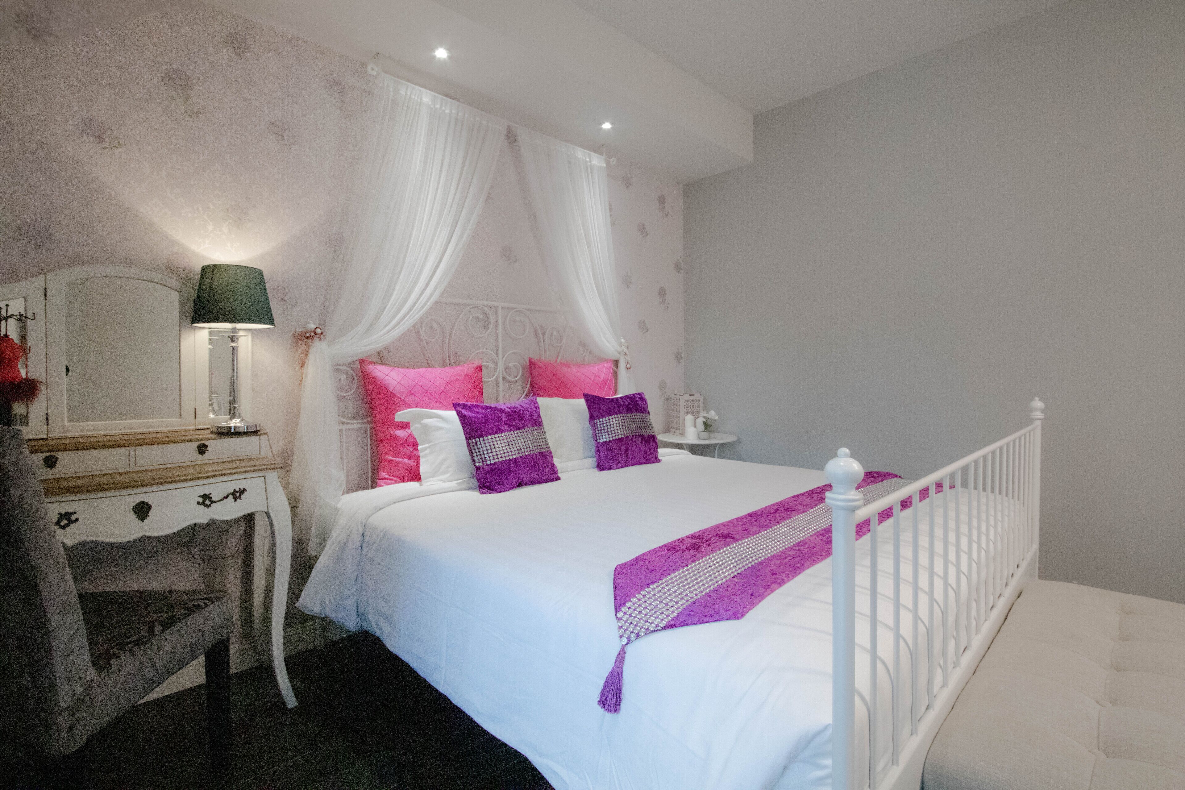 Une chambre à coucher avec un lit blanc, une table de chevet avec une lampe, une chaise et un mur décoratif.
