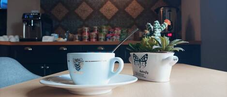 A table with a coffee cup and saucer, a butterfly-themed mug, and a small potted plant.