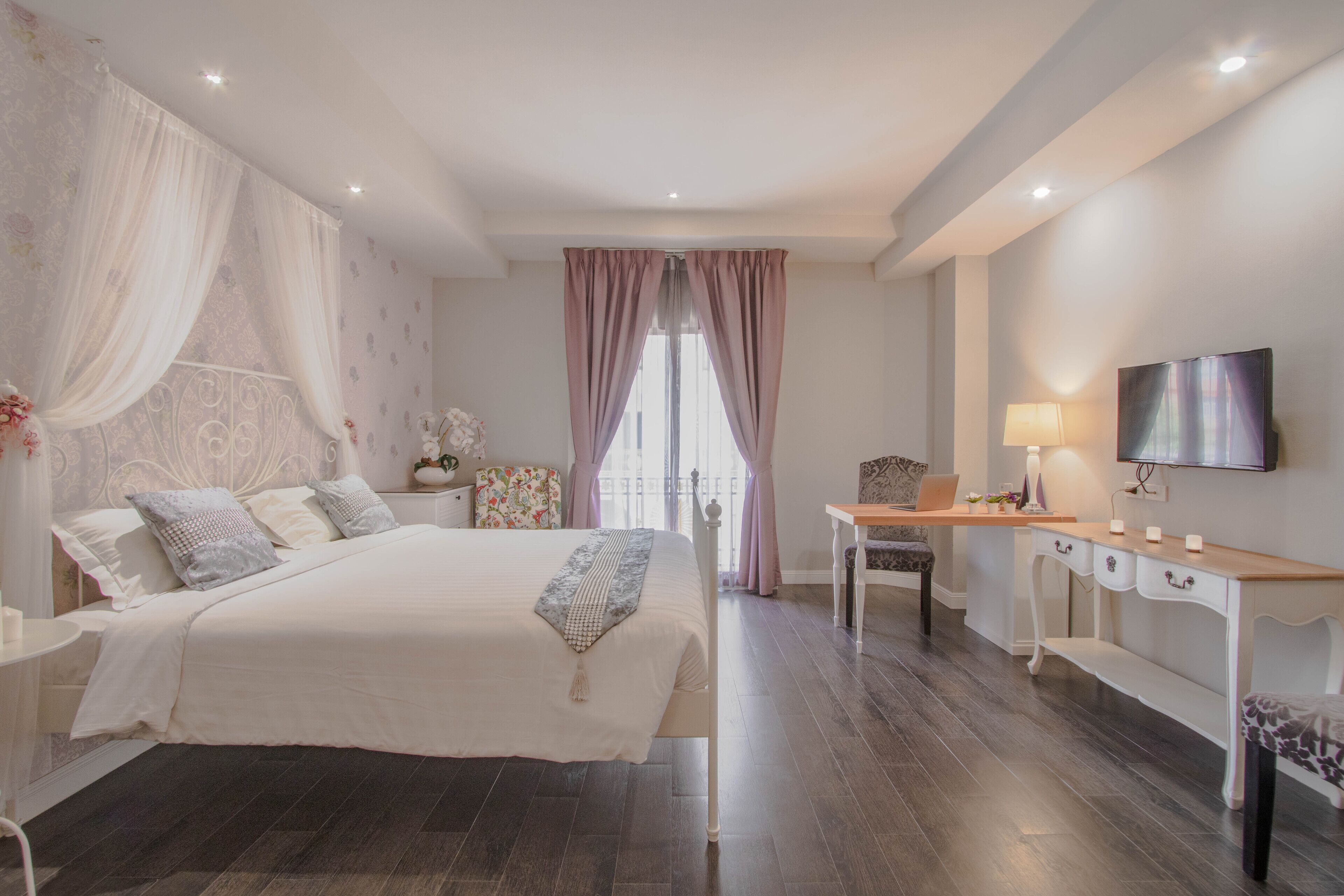 A bedroom with a bed, bedside table, lamp, TV, and a desk with drawers.