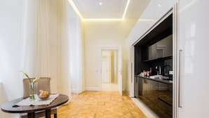 A modern hotel room with a dining area, a kitchen with a black countertop, and a patterned wooden floor. - Residence Wollzeile (Vienna)