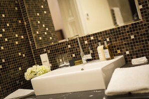 A modern bathroom with a large mirror, black mosaic tiles, a white sink, and a vase of white flowers. - Residence Wollzeile (Vienna)
